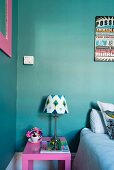 Pink bedside table and lamp with patterned lampshade against turquoise wall