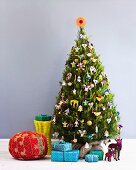 Red pouffe, wrapped presents and animal ornaments under Christmas tree decorated with many different figurines