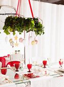 Weihnachtlich dekorierter Kranz von Decke abgehängt über gedeckten Tisch mit roten Retro Weingläsern