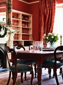 Antique wooden table in front of ornate open fireplace, heavy silk curtain and red walls