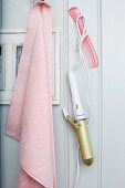 Pink towel and retro curling iron hanging from hooks on white wooden wall