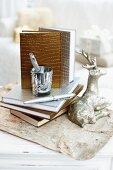 Note books with gold and silver mock-croc bindings next to silver reindeer ornament and writing utensils on vintage paper