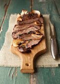 Sliced Flank Steak with Onions and Mushrooms on a Cutting Board