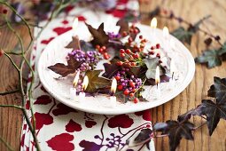 Wreath of callicarpa, tiny rosehips and purple ivy surrounded by small candles on plate