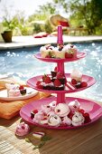 A tiered cake stand holding individual cakes and treats by a swimming pool