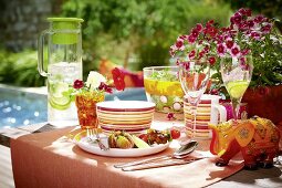 A table laid for a meal with lemonade, fruit and salad by a swimming pool