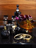 Various elegant perfume bottles, bowl of orchid flowers and bracelets on black dressing table