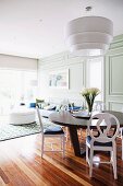 Dark wooden table and white painted chairs in open-plan interior with ship deck flooring and classic wood panelling