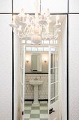 View though open, lattice, double doors into bathroom with pedestal basin; white, wallpapered, fitted cupboards and chandelier in foreground