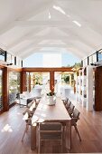 Dining area in long, hall-like interior with exposed roof structure and glass walls on three sides