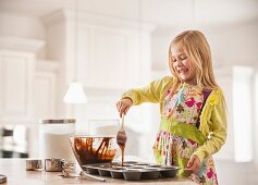 Mädchen gibt Schokoladenteig in eine Muffinform