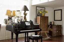 Antique table lamps on grand piano in front of window next to antique chests of drawers