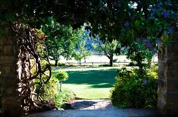 Opening in stone wall leading to large lawn edged by row of trees