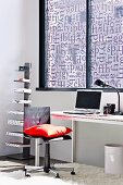 Office chair with red cushion and minimalist desk below window with screen printed with letters