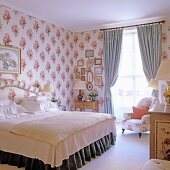 Bedroom with fabric wall covering, double bed & upholstered armchair in front of window with draped curtains