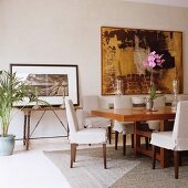 Loose-covered chairs at long table in exotic wood and modern artwork on wall in classic, elegant dining room