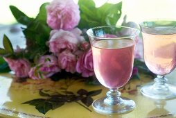 Rose syrup in two glasses, in the background a bunch of roses