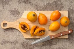 Medlars, whole and halved, on a chopping board