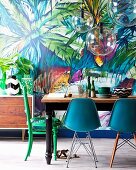 Dining table, various chairs and spherical glass lamps in front of jungle patterned wallpaper