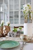 Festive table decoration with hyacinths and hellebores in original containers combined with crystal glasses and floral cups