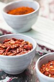 Whole, dried chilis and chili powder in dishes on a colorful wooden surface