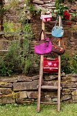 Various hand-made felt bags hanging from ladder against stone wall