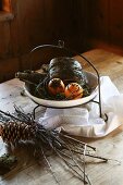 Advent arrangement of oranges stuck with cloves in dish on metal frame with hook next to twigs and fir cones on table