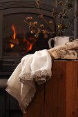 White linen cloth with crocheted hem and logs on wooden block in front of fire in wood-burning stove