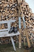 Vintage skiing equipment on weathered wooden bench in front of firewood stacked against house facade