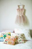 Kissen mit fröhlichem Blumenmuster auf Bett und aufgehängtes Ballettkleid an Wand