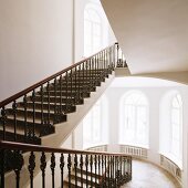 Grand stairwell - wrought iron balustrade on staircase and tall arched windows on landing