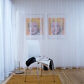 Weisser Schalenstuhl neben Stehleuchte vor transparentem Vorhang und Blick auf Portrait von Marilyn Monroe