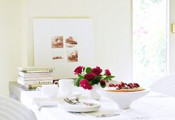 A table laid with strawberry cake, a bunch of roses, a coffee service and books