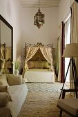 Moroccan bedroom in shades of cream with sofa, canopied bed and lantern-shaped ceiling lamp