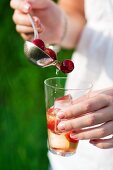 A woman pouring cherry cooler from a ladle into a glass