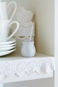 Edge of kitchen shelf decorated with lace ribbon; napkin rings of starched lace trim in background
