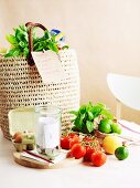 A wicker shopping bag with a list, tomatoes, limes, eggs, coins, a notebook and a pen