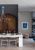 Set, modern dining table below designer pendant lamp in front of antique cupboard against grey wall