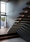 Floating stair treads protruding from wall in minimalist stairwell with open terrace door