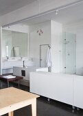 White sideboard on castors next to open-plan bathroom area in loft-style interior