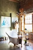 Freistehende Vintage Badewanne unter Kronleuchter in rustikalem Bad mit Estrichfussboden