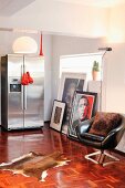 Black vintage leather armchair and animal-skin rug on mosaic parquet floor; stainless steel, side-by-side fridge freezer against wall