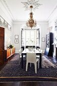 Black table and white chairs below chandelier and stucco elements on ceiling in eclectic dining room