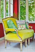 Antique Louis XVI sofa with yellow velvet cover and patterned scatter cushions below windows in corner with red-painted walls
