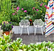 Durchbrochene, weiße Schalensessel auf Terrasse vor Blumenbeet; im Vordergrund gestreifter Sonnenschirm