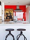 Vintage Drehhocker mit Metallgestell vor weisser Theke in offener Küche und Blick auf Mona Lisa Bild an roter Glaswand