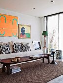 Rustic wooden coffee table on sisal rug in front of pale couch with zebra-patterned scatter cushions and artworks on wall