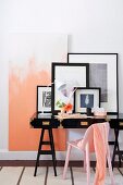 Pastel pink scarf on chair of same colour in front of black-framed pictures on black-painted writing desk