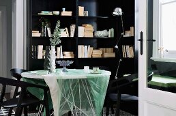 Blick durch offene Tür auf Tisch mit transparenter Tischdecke und schwarze Stühle vor schwarzem Einbauregal