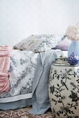 Detail of a boudoir - Side table painted with flowers and birds next to bed with bedspreads and throws